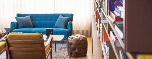 Shows living room with a blue couch against window and large book shelf to the right