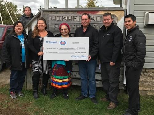 Shows 7 people outside holding a large cheque from McDougall Energy