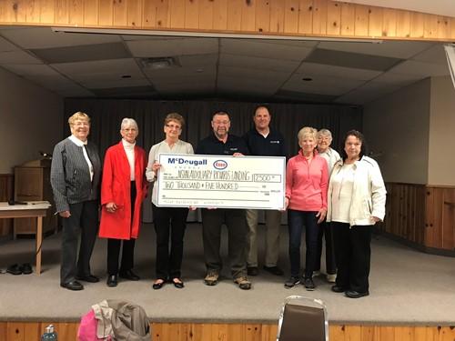 Shows 8 people on a stage holding a large cheque from McDougall Energy