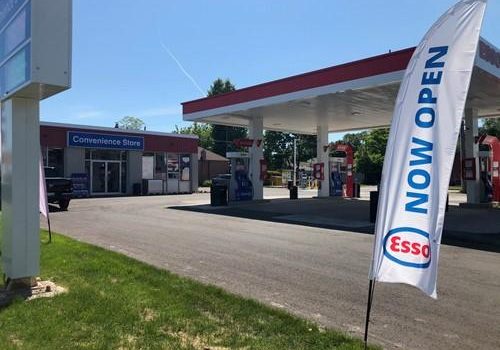 Shows exterior shot of Esso gas station with a large stake banner with words Esso Now Open