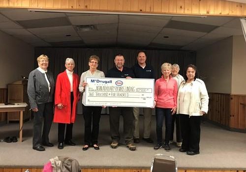 Shows 8 people on a stage holding a large cheque from McDougall Energy